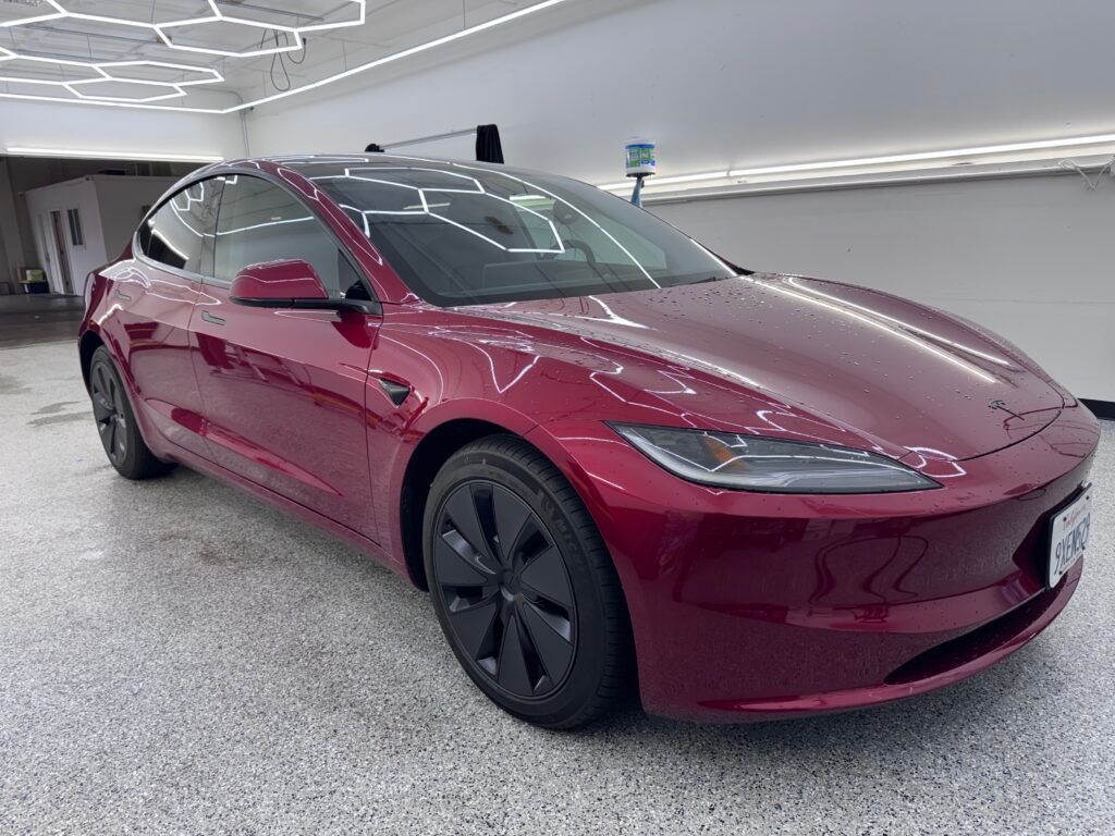 Maroon Tesla sedan in a modern parking garage with white ceiling lights