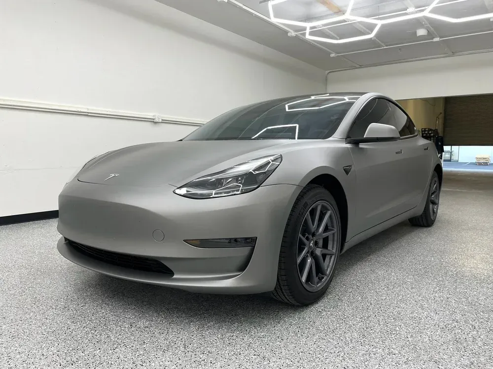 Matte gray Tesla Model 3 parked in a garage, front three-quarter view.