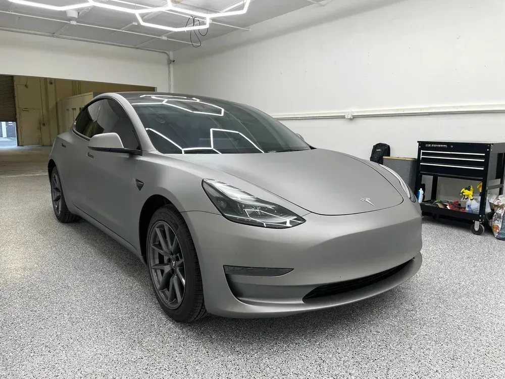 Silver Tesla sedan parked in a garage with a tool cart and bright ceiling lights