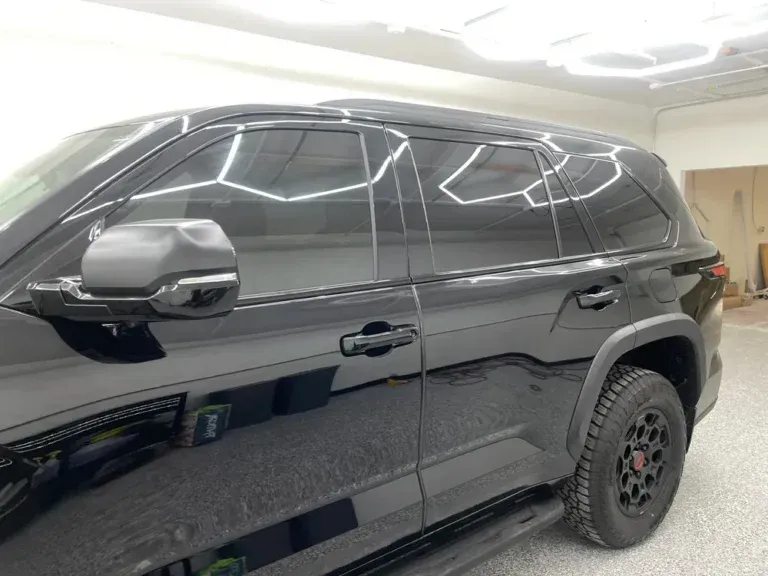 Black SUV parked indoors under bright ceiling lights, side view with tinted windows and black wheels