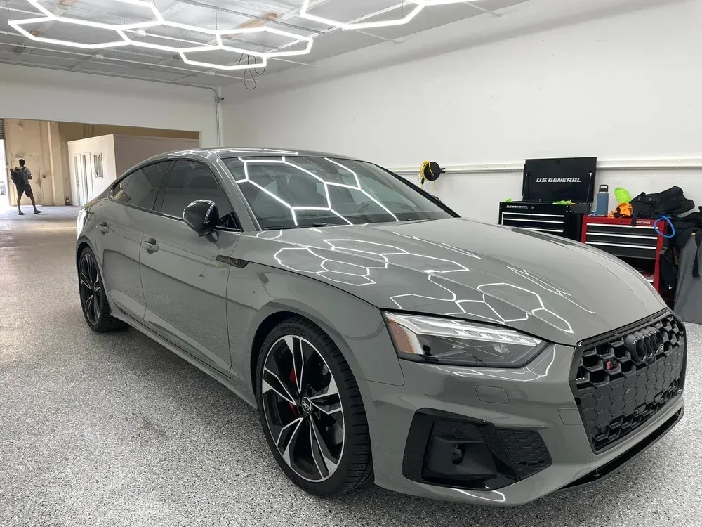 Gray sporty sedan in a bright garage showroom, angled front view with black wheels and red brake calipers