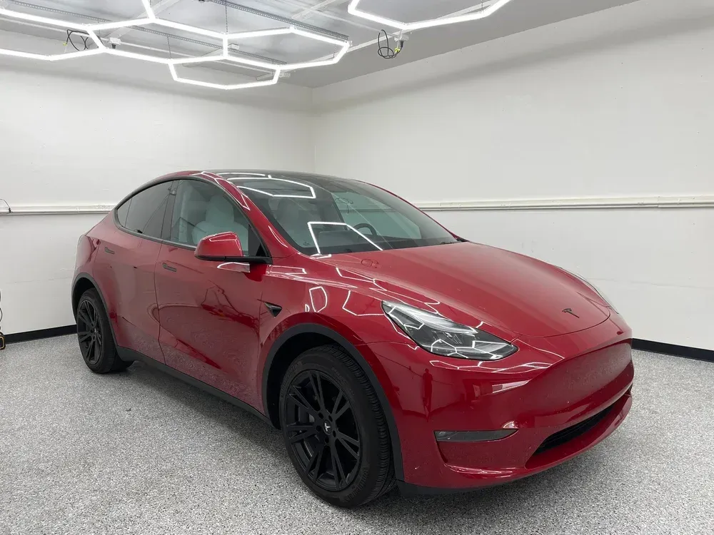 Red Tesla Model Y in a white showroom with hexagonal ceiling lights.