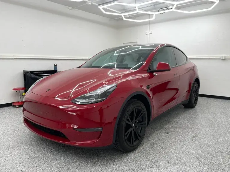 Red Tesla Model Y in a white garage, front-left view, with black wheels.