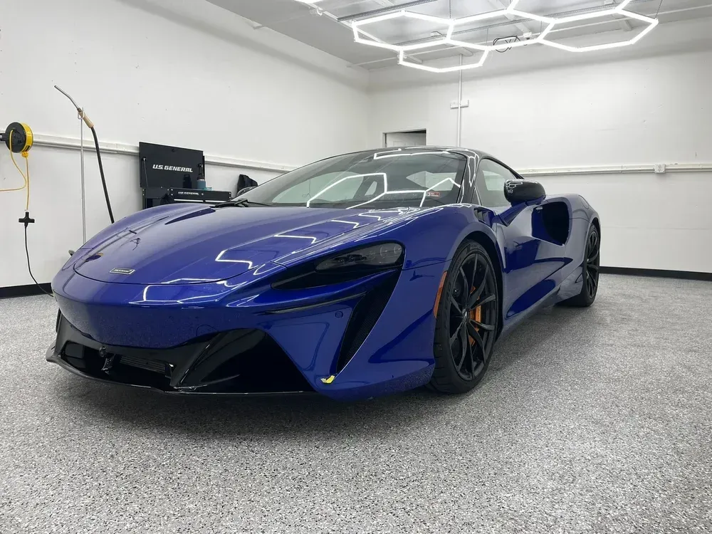 Blue sports car parked in a modern garage with hexagon ceiling lights and gray floor