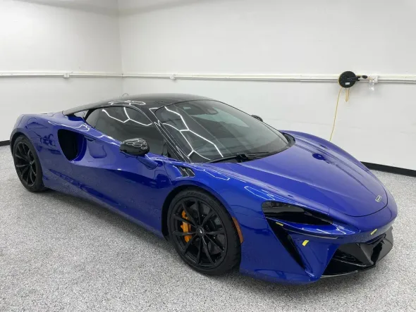 Blue sports car parked in a white garage, front three-quarter view.