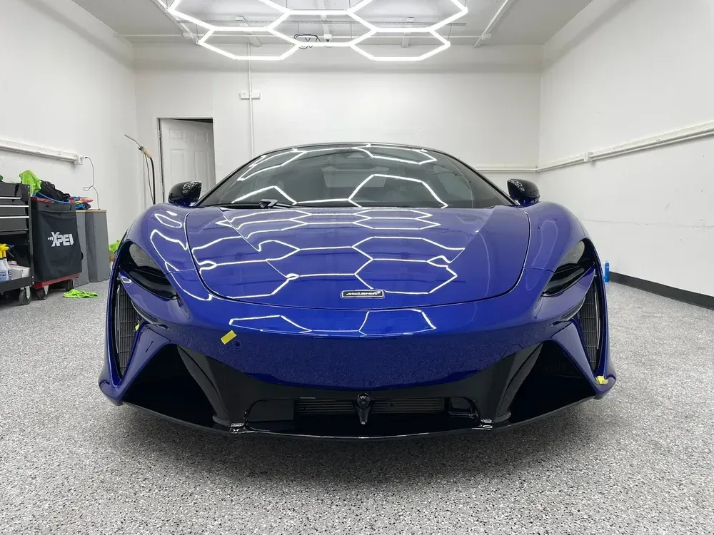 Blue sports car in a white showroom, front view under bright ceiling lights