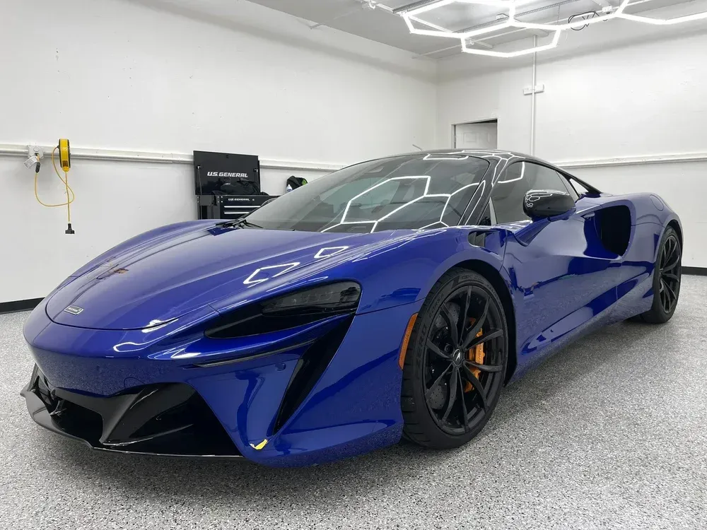 Blue sports car in a white showroom, shown from the front-left angle.