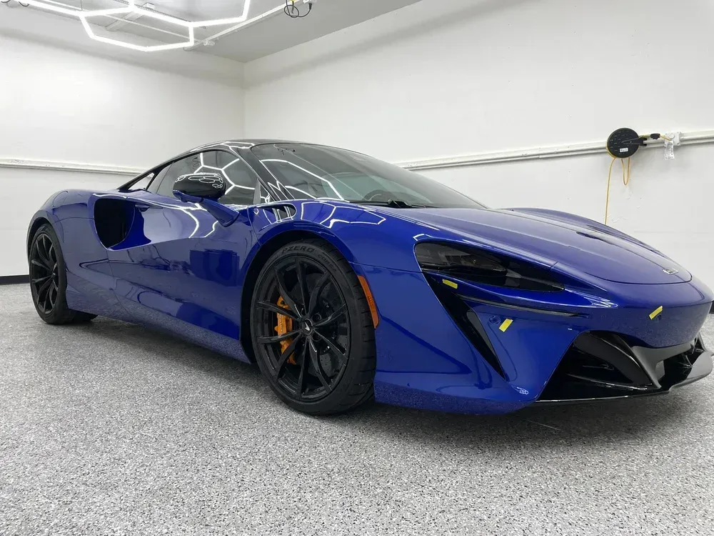 Blue sports car parked in a bright garage, viewed from the front-left side.