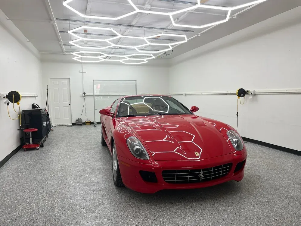 Red sports car parked in a bright garage with geometric ceiling lights.