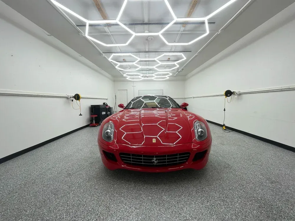 Red sports car centered in a bright garage with hexagonal ceiling lights