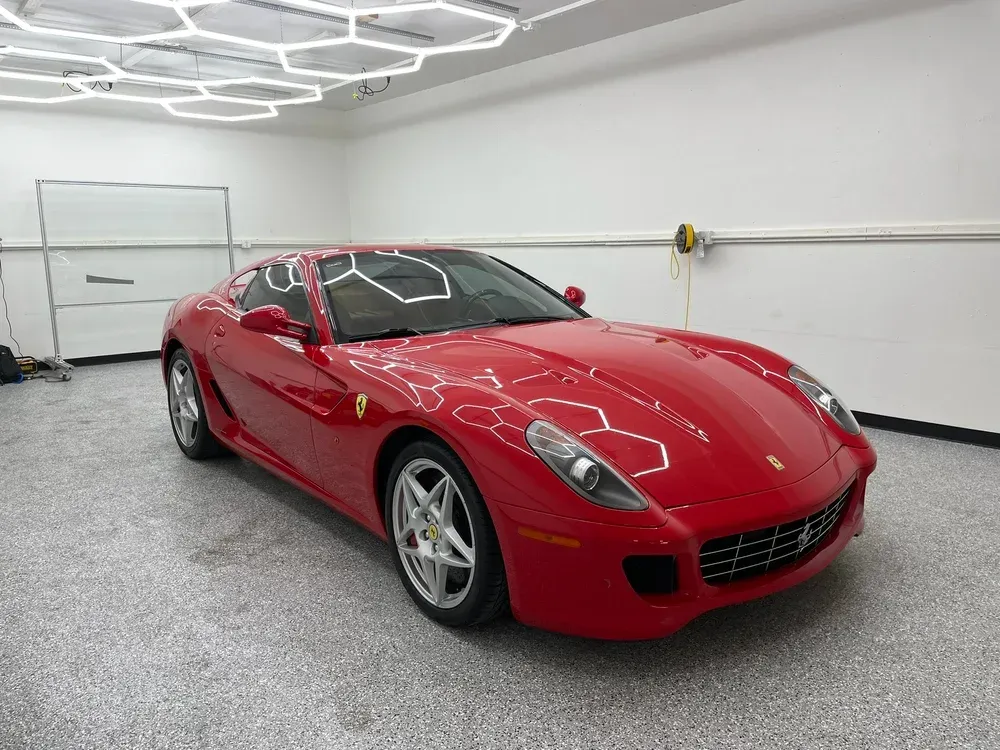 Red sports car parked in a bright garage with white walls and ceiling lights.