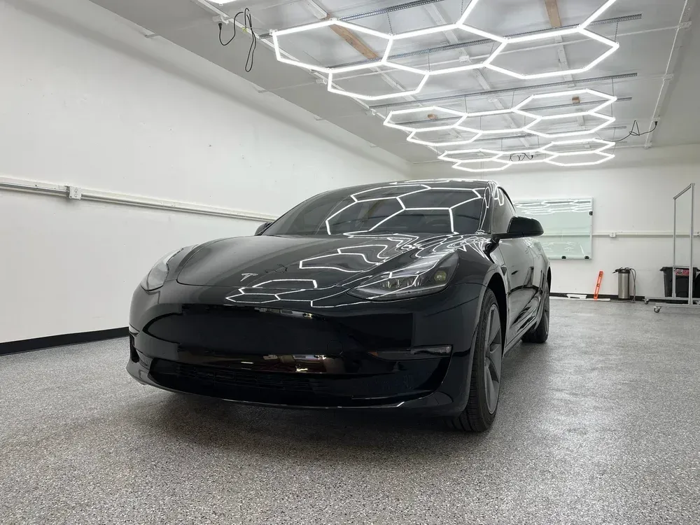 Black sports car in a bright modern garage with geometric ceiling lights.