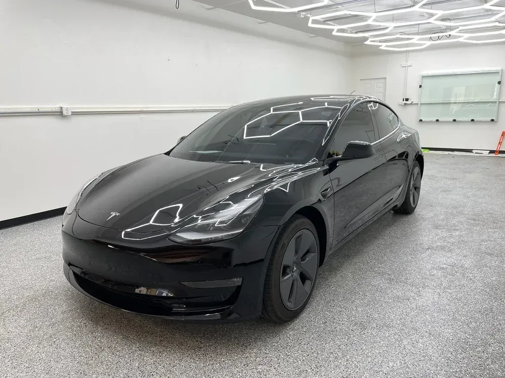 Black Tesla sedan parked in a bright showroom with white walls and ceiling lights