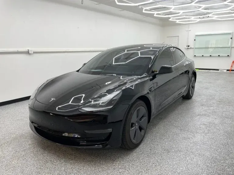 Black Tesla sedan parked in a bright showroom with white walls and gray floor
