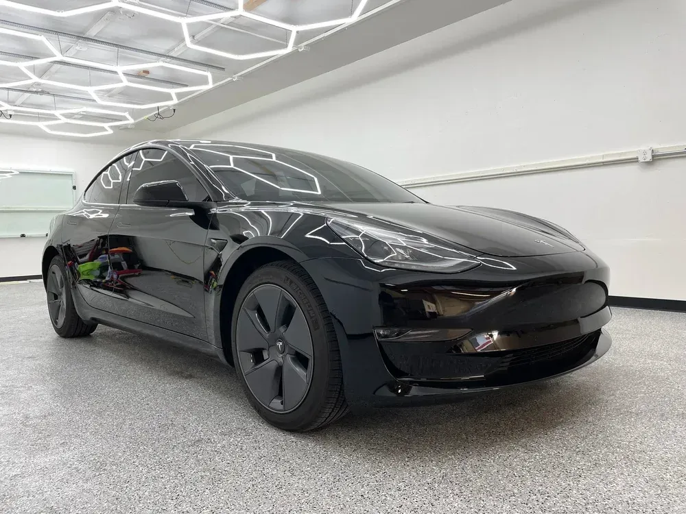Black Tesla sedan in a showroom with bright geometric ceiling lights