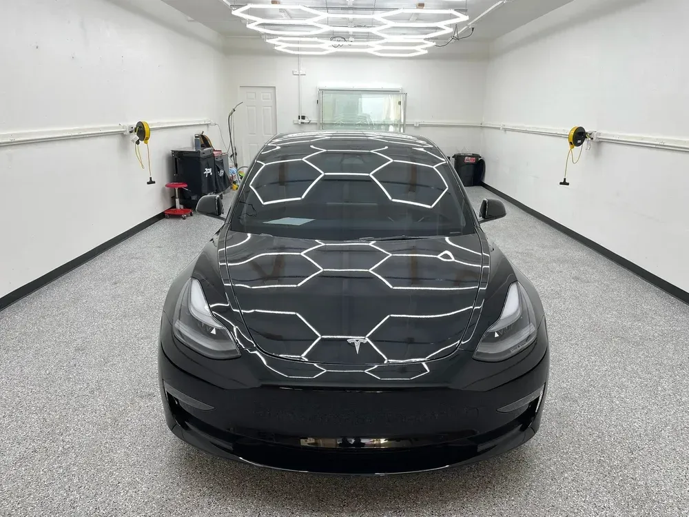 Black Tesla in a white garage with geometric ceiling lights reflecting on the hood