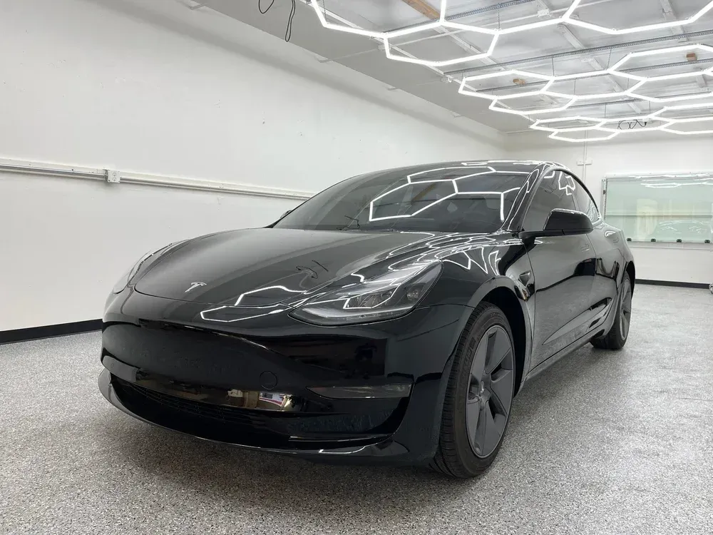 Black Tesla sedan in a bright indoor showroom, front three-quarter view