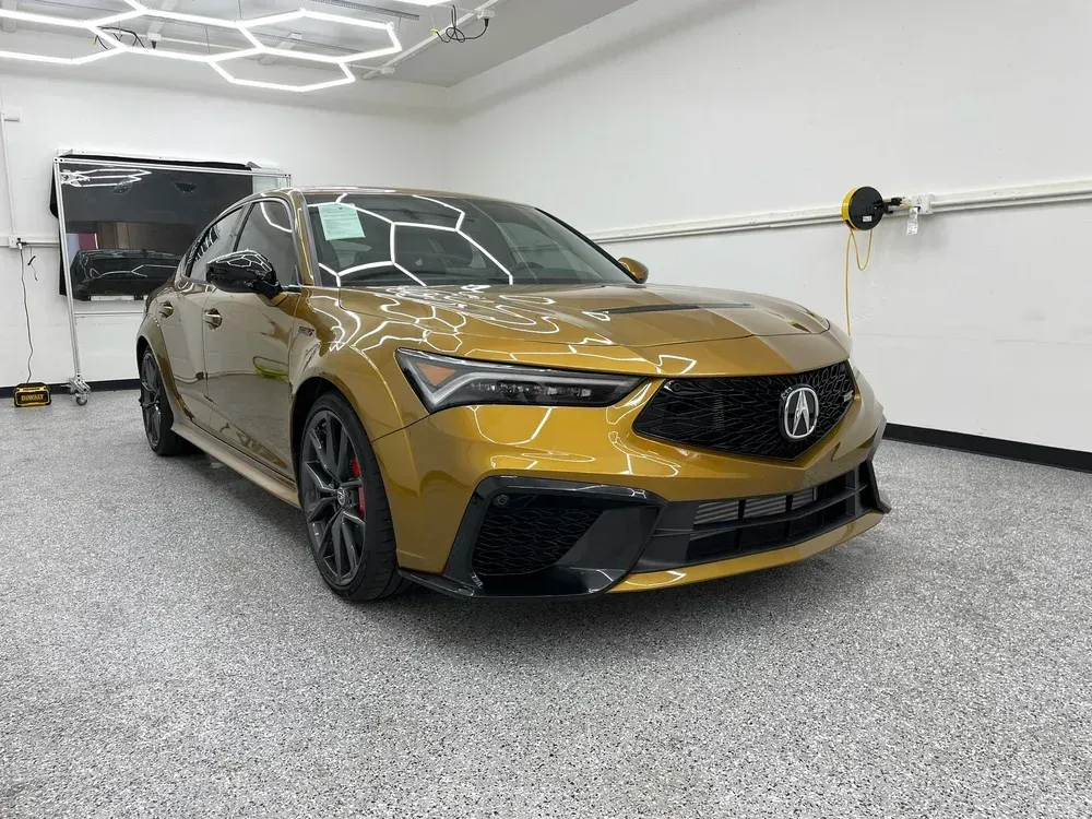 Gold Acura SUV in a modern garage, viewed from the front-left with geometric ceiling lights overhead