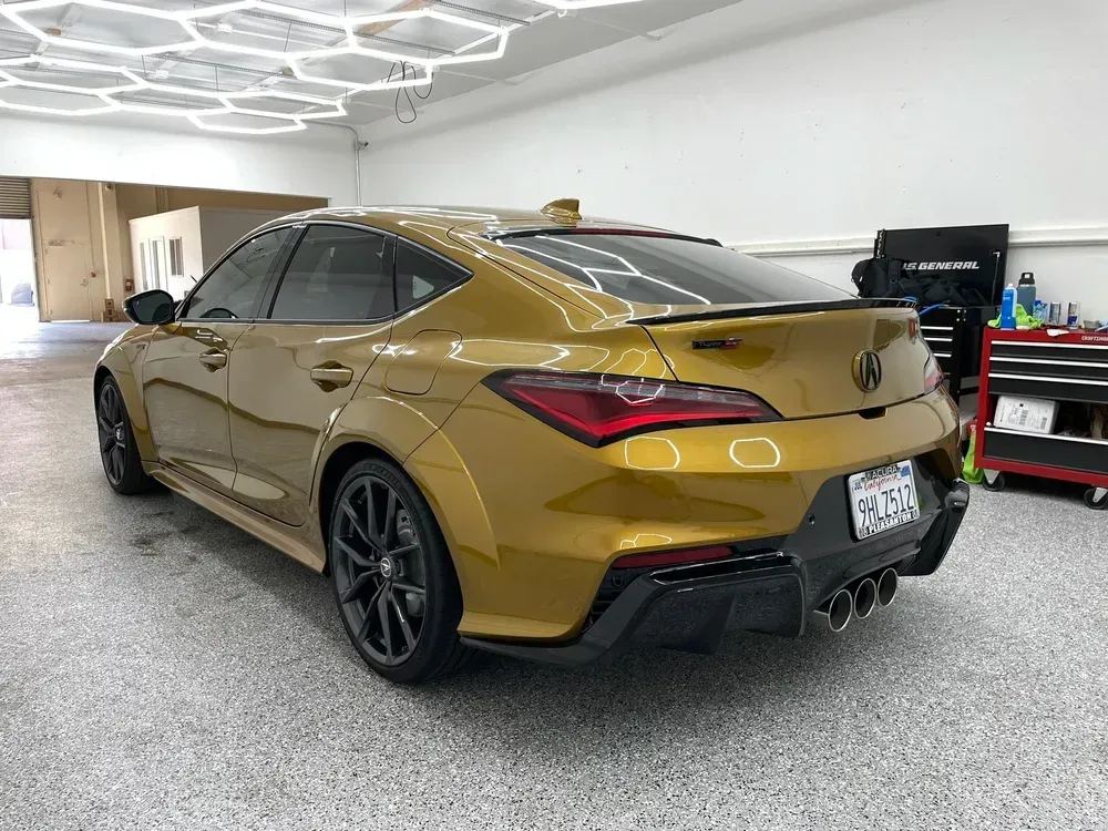 Gold sedan parked in a garage, rear three-quarter view with black wheels and spoiler
