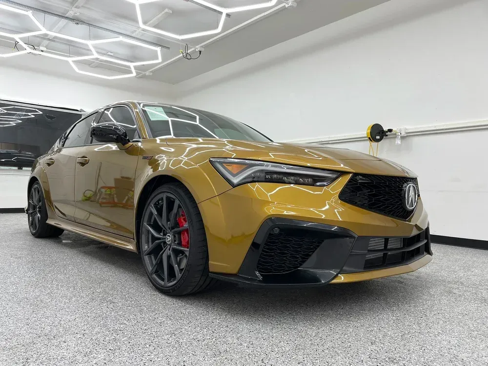 Gold sports sedan in a showroom, shot from the front-left with black accents and red brake calipers.