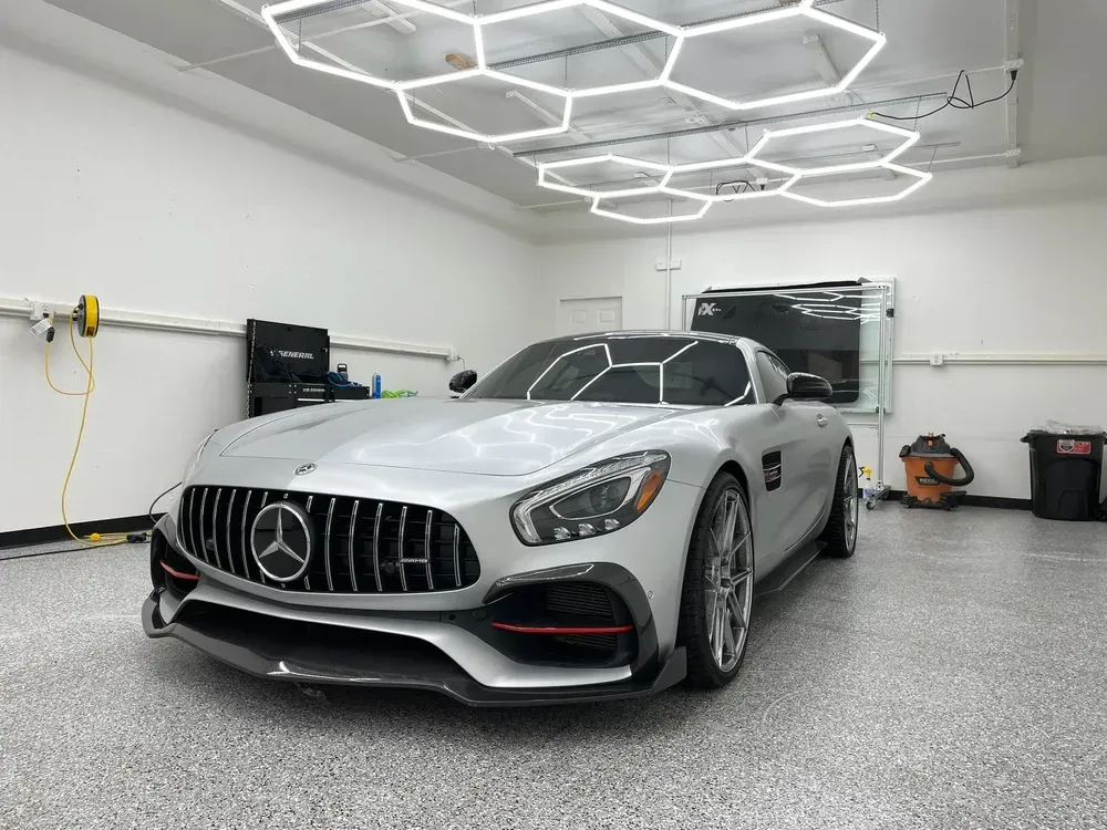 Silver Mercedes-AMG sports car parked in a modern garage under hexagonal ceiling lights