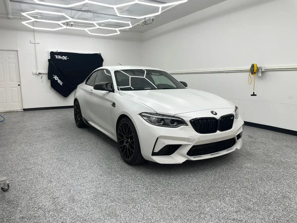 White BMW coupe in a clean garage with hexagon ceiling lights and gray speckled floor