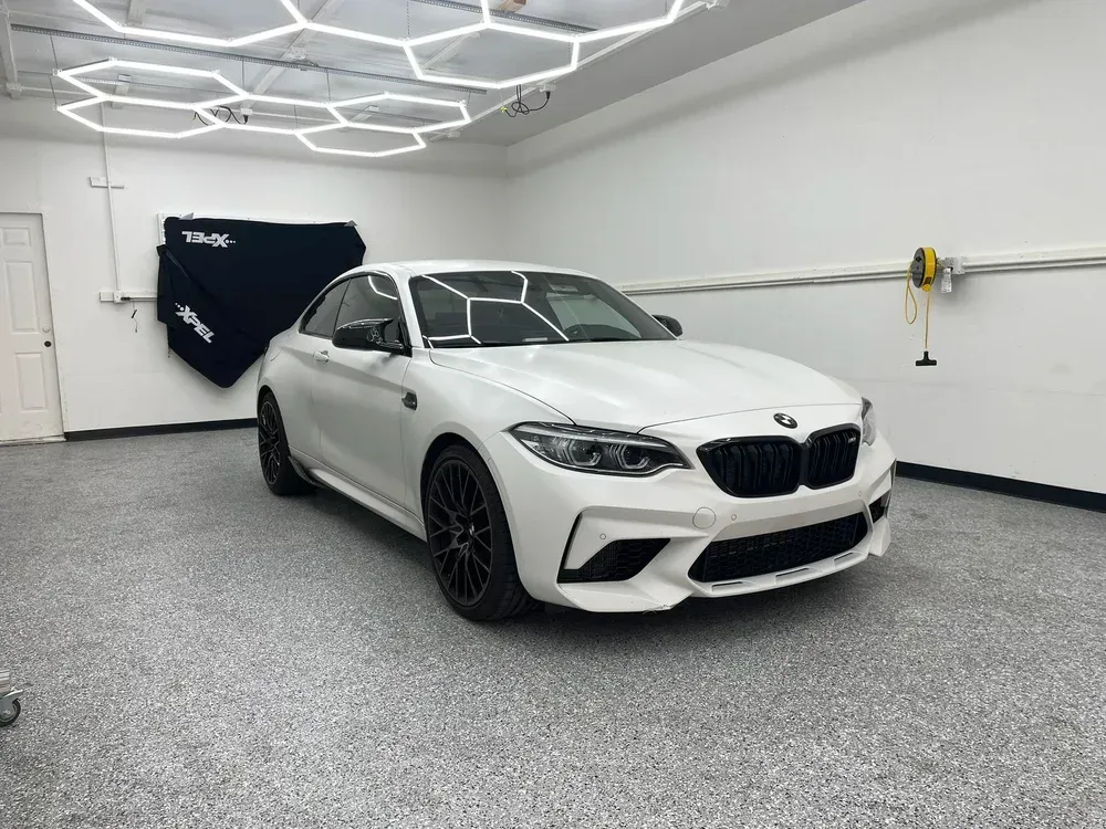 White BMW coupe in a clean garage with bright hexagon ceiling lights.