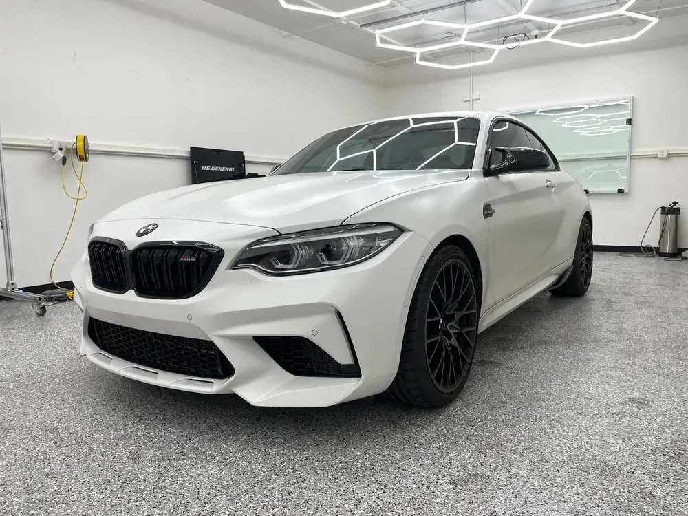 White BMW sedan in a clean garage with hexagon ceiling lights and black wheels