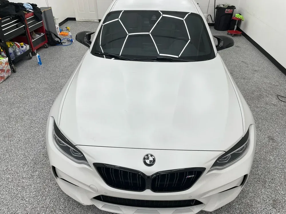 White BMW sports car parked in a garage with a black geometric sunshade on the windshield