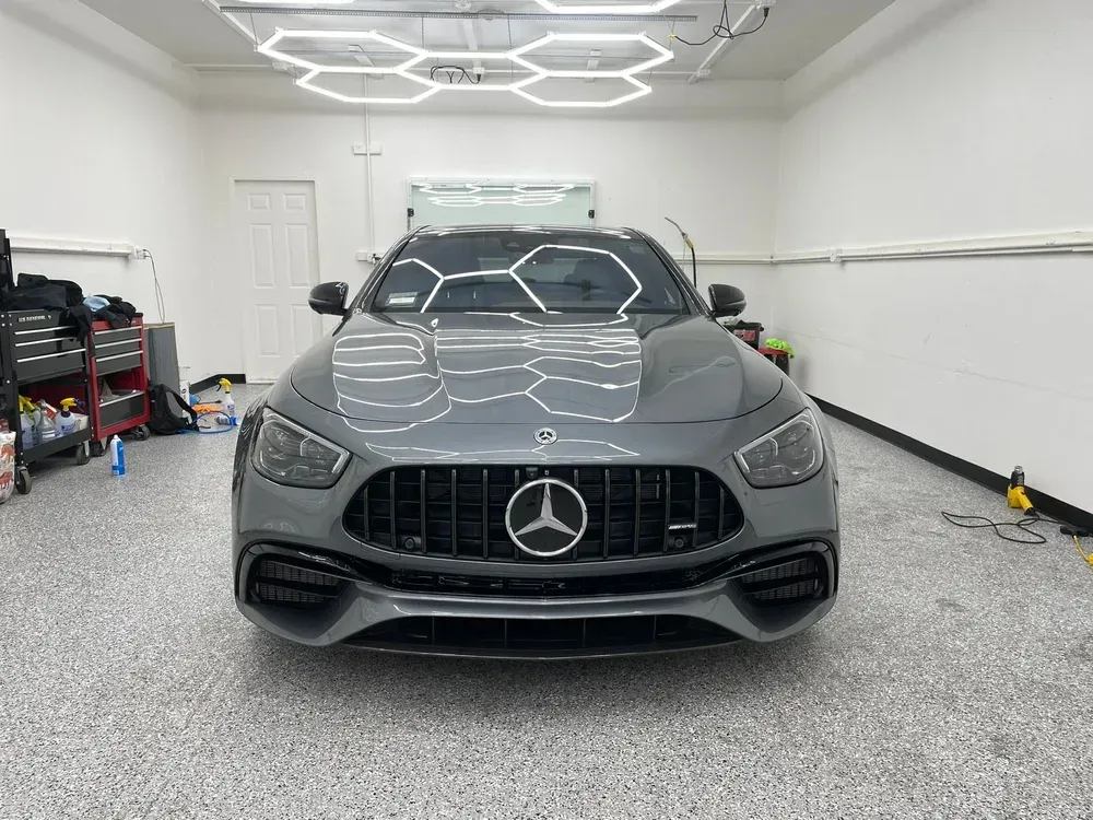 Gray Mercedes-Benz sedan in a garage, front view under bright ceiling lights.