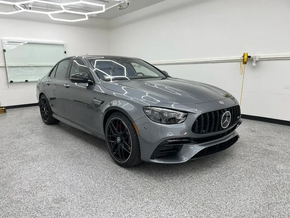 Gray Mercedes-AMG sedan parked in a bright garage with white walls and a speckled floor