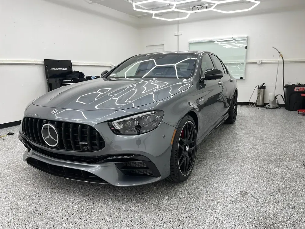 Gray Mercedes-Benz sedan in a bright showroom with glossy floors and ceiling lights