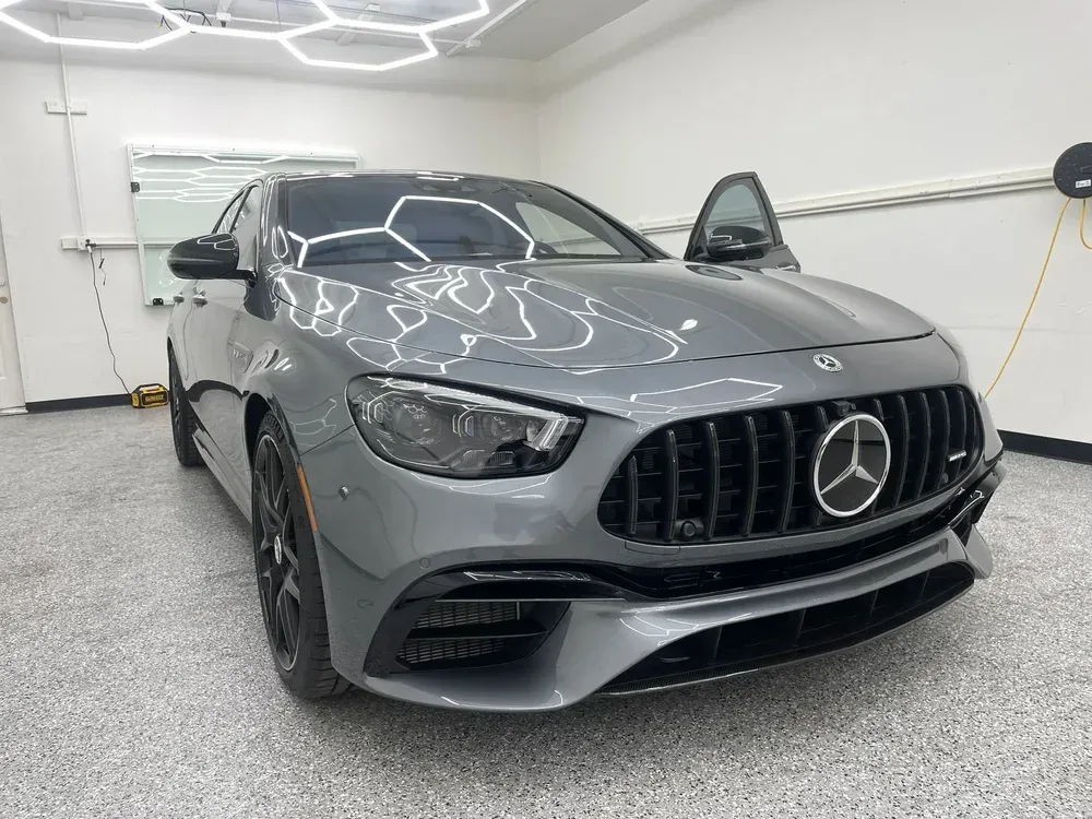 Gray Mercedes sedan in a bright garage, front view with the driver's door open and overhead light reflections.