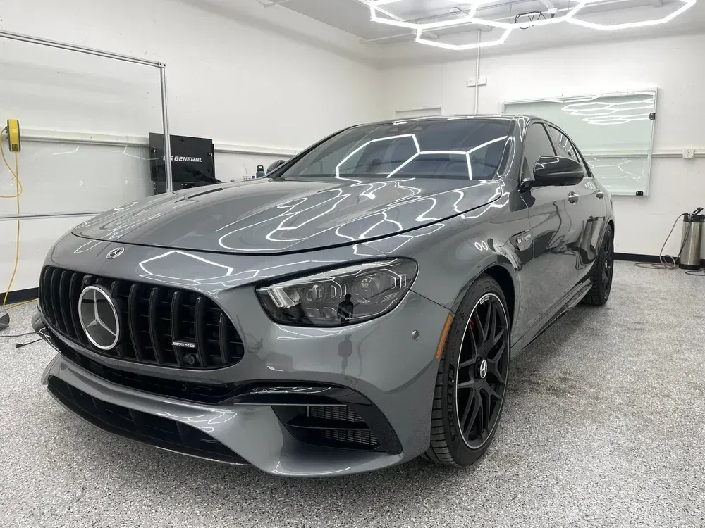 Gray Mercedes-Benz AMG sedan in a bright garage, front-left view with black rims and large grille