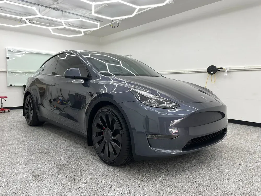 Dark gray Tesla Model Y in a bright garage with white geometric ceiling lights
