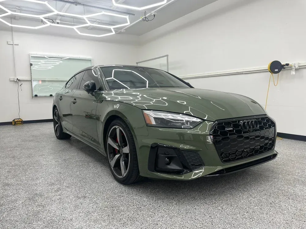 Olive green sedan in a bright garage, shown from the front-left angle