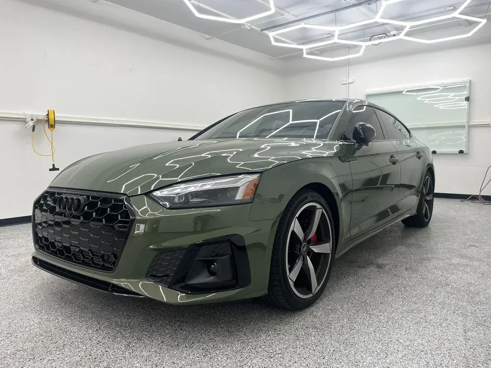 Dark green sports sedan in a bright showroom with geometric ceiling lights.
