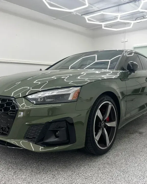 Dark green sports coupe parked in a bright showroom with geometric ceiling lights.
