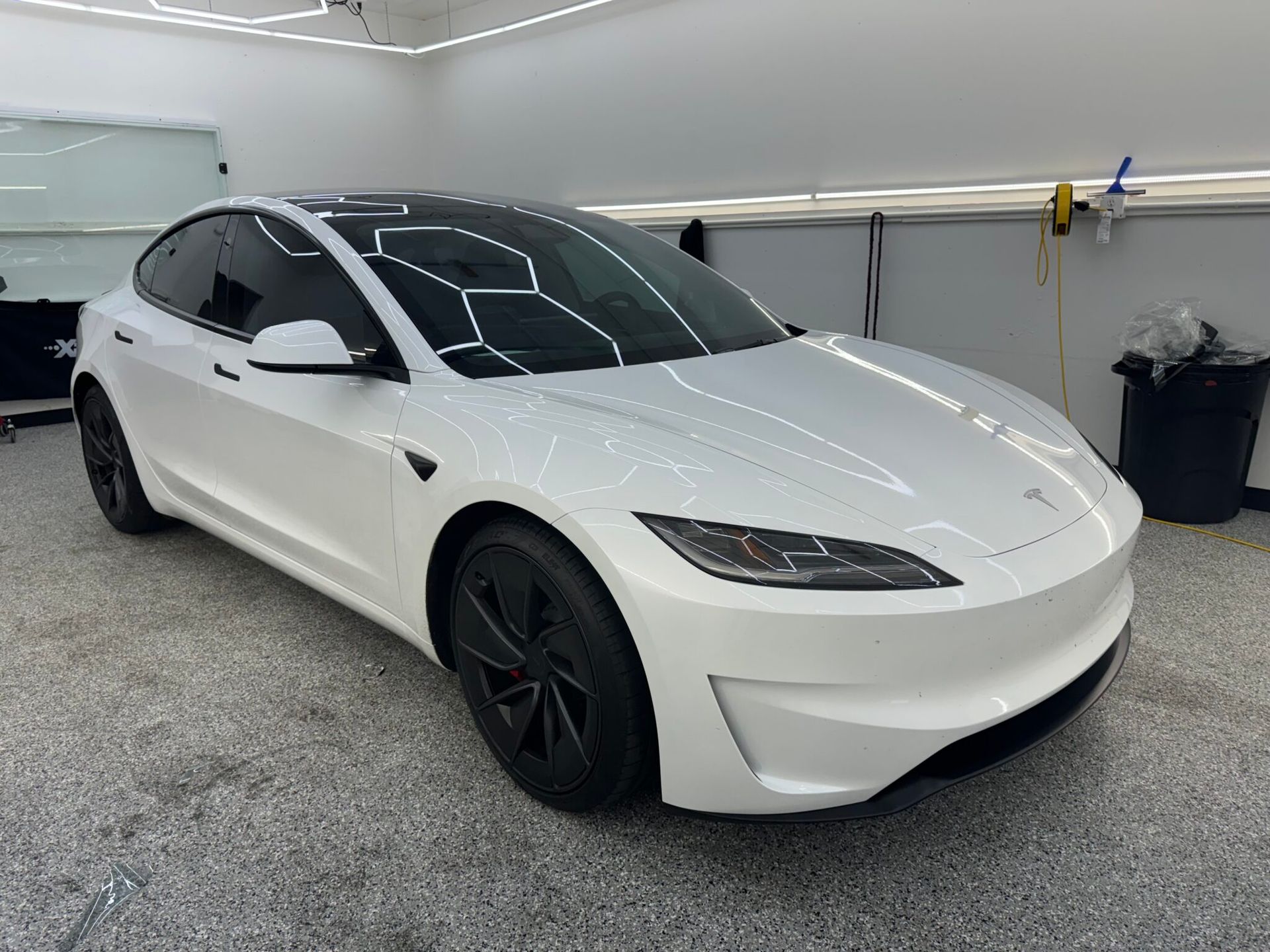 White Tesla sedan parked indoors on a gray floor, front three-quarter view