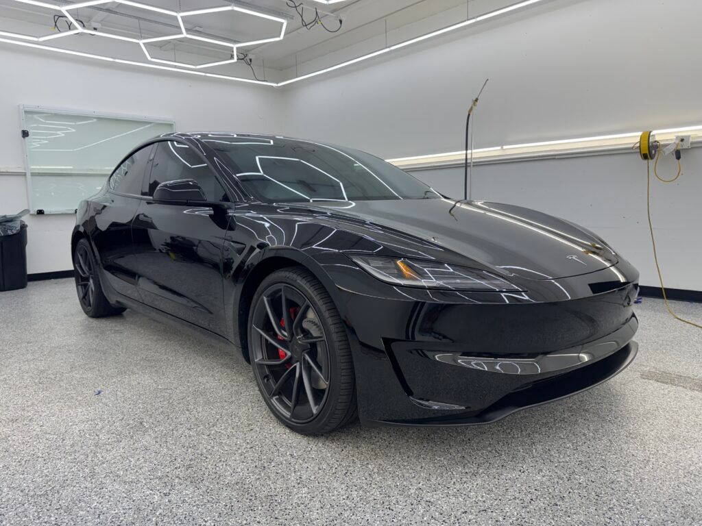 Black sports car in a bright garage, viewed from the front-left side.