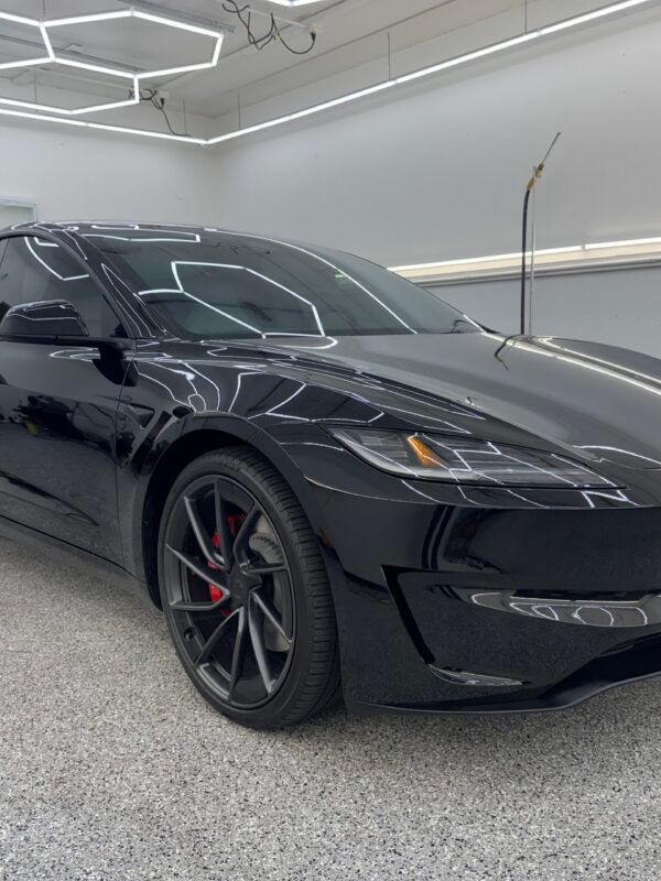 Black sports car in a modern garage with geometric ceiling lights and red brake calipers