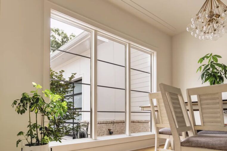 Bright dining area with large windows, white chairs, potted plants, and a chandelier