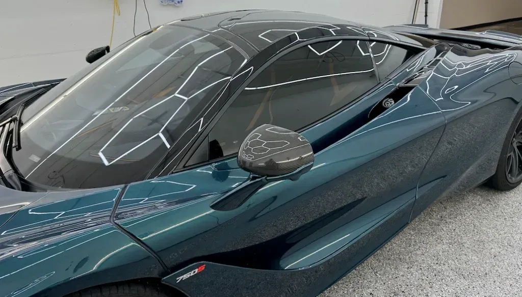 Teal sports car with black roof and side mirror, photographed indoors under bright lights