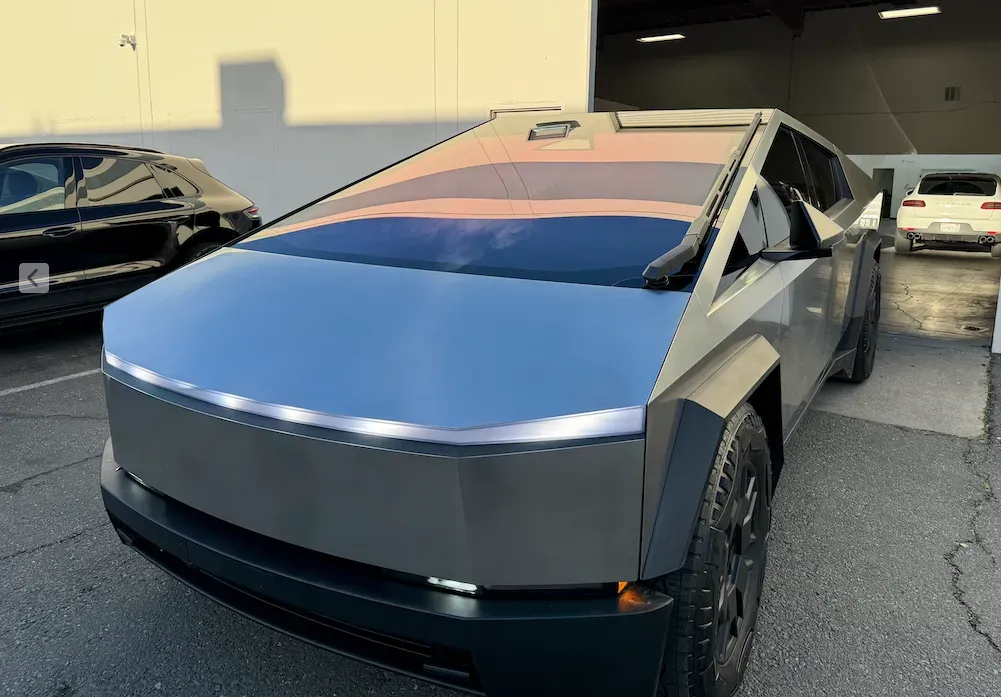 Silver Tesla Cybertruck with blue and orange wrap parked outside a building under construction.