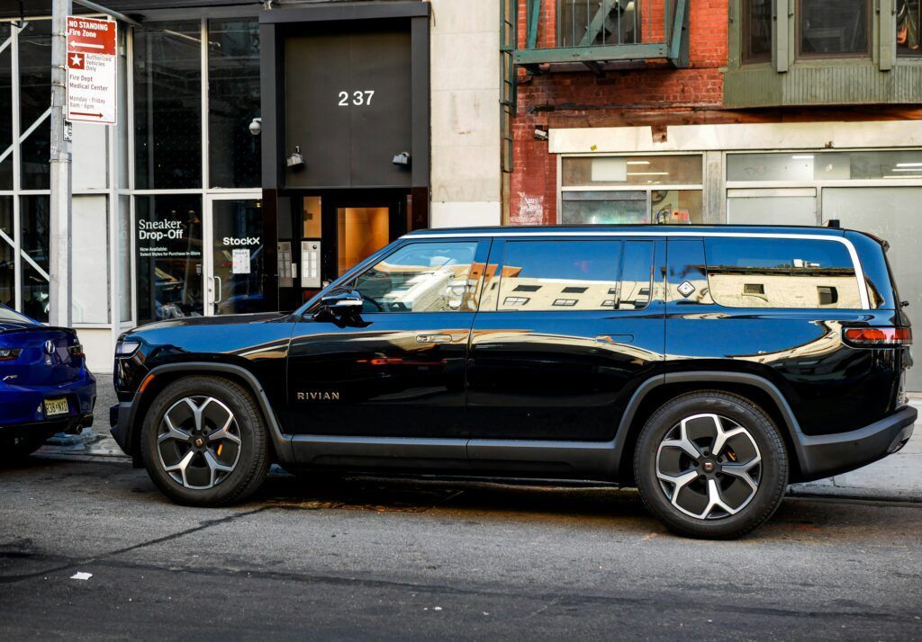 Black SUV parked on a city street beside a brick building, with reflective windows and a blue car nearby