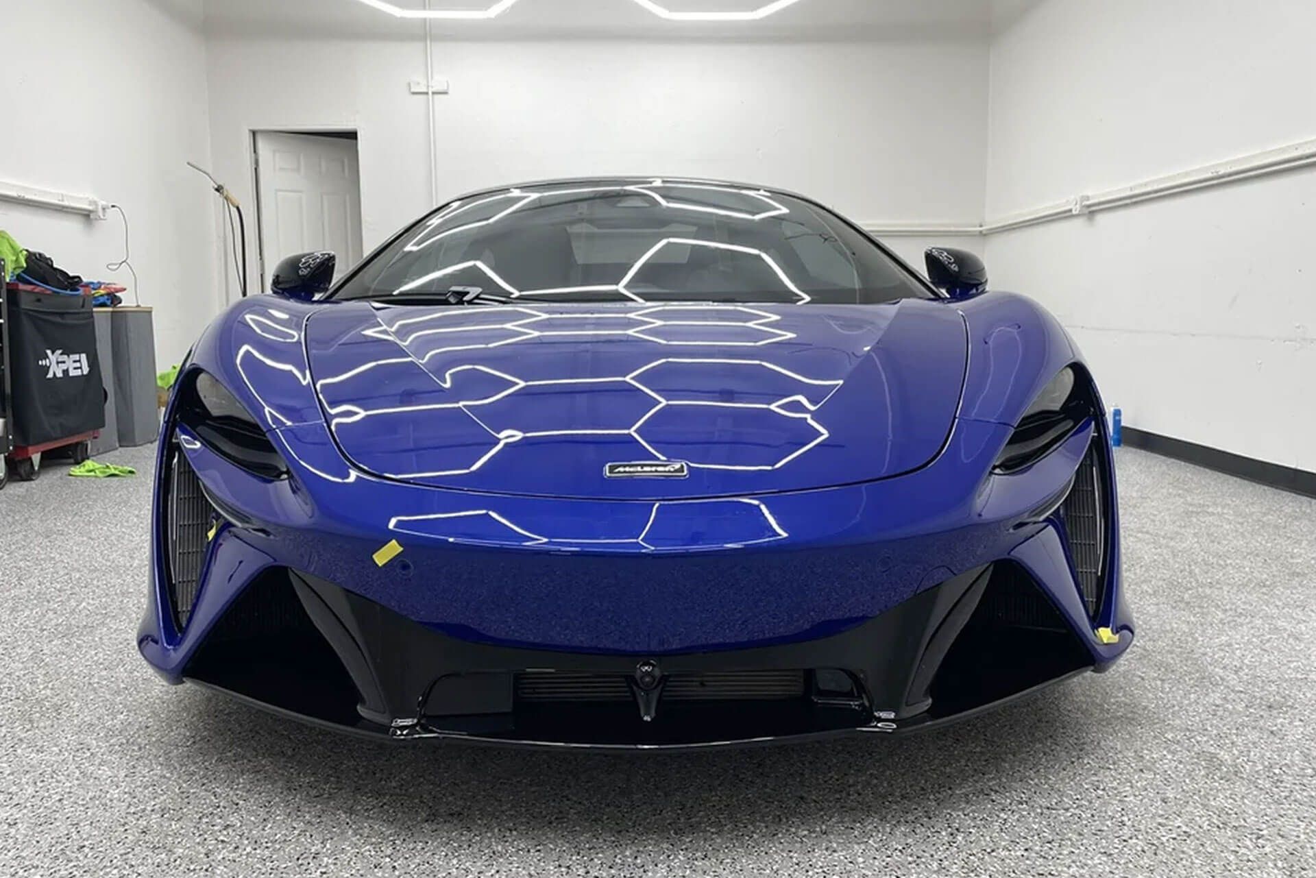 Blue sports car parked in a white garage, seen from the front.
