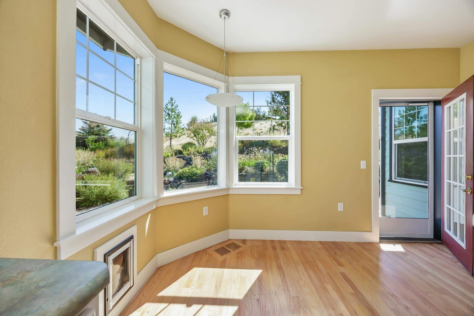 Bright empty room with bay windows, yellow walls, wood floor, and an open door to a balcony.