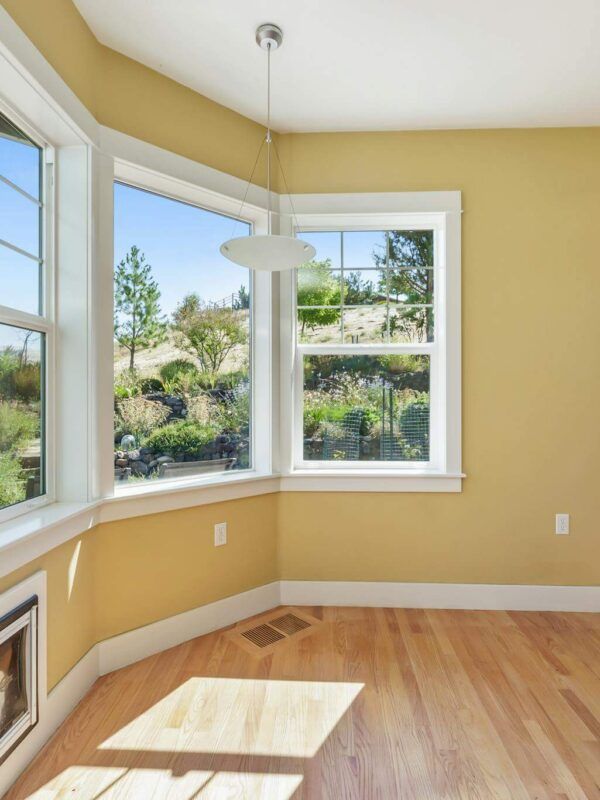 Bright empty room with large windows, yellow walls, and sunlit hardwood floors