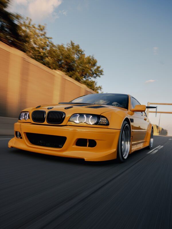Orange BMW sports car driving on a road, low-angle motion shot at sunset