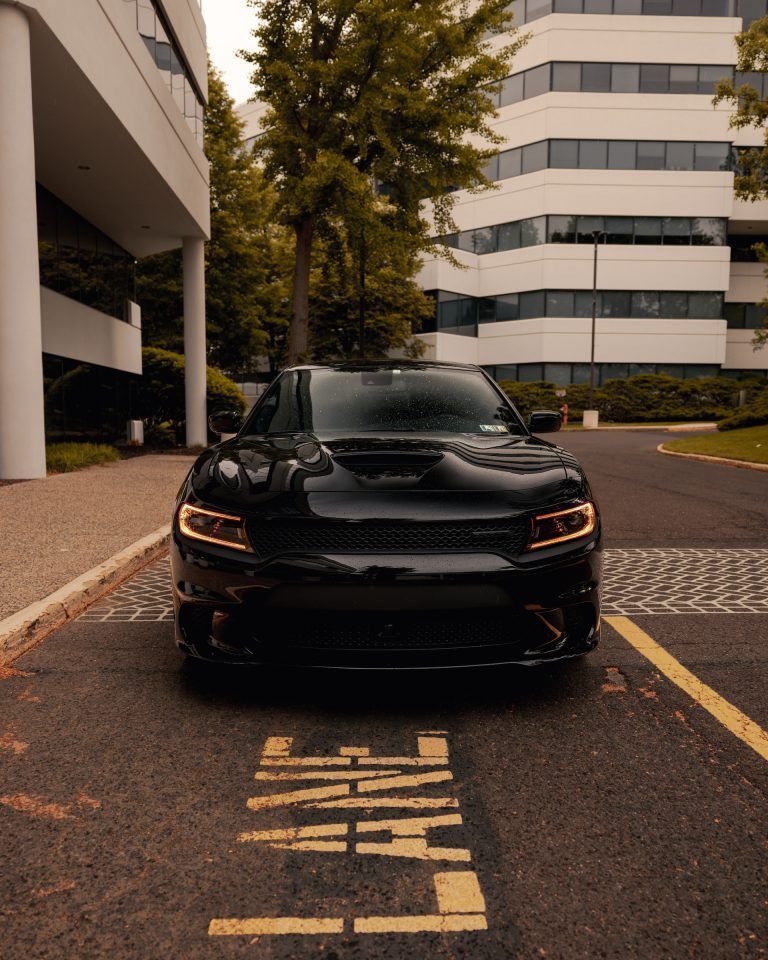 Black sports car parked on a city street between modern office buildings.